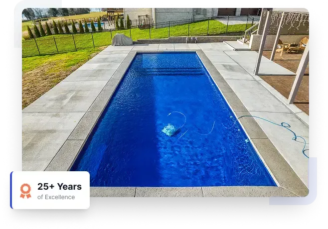 Rectangular blue backyard swimming pool with stone decking and a pool cleaner floating inside