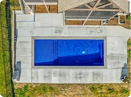Aerial view of a rectangular backyard pool with blue water, concrete deck, and patio furniture nearby