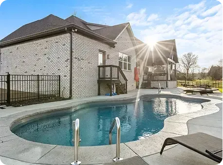 Backyard with a freeform swimming pool beside a brick house at sunset