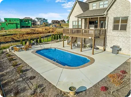 Backyard patio with an in-ground pool beside a two-story house and wooden deck.
