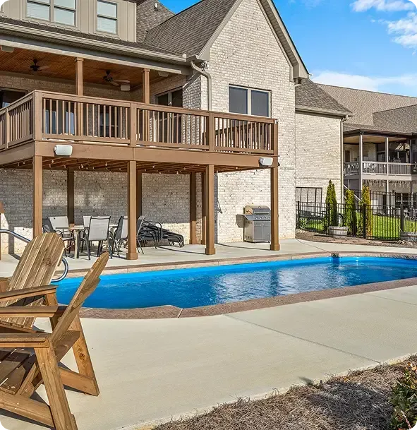 Backyard pool beside a two-story house with a wooden deck and patio chairs