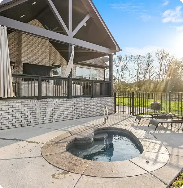 Patio with a small oval fire pit beside a covered deck and outdoor seating, overlooking a grassy yard