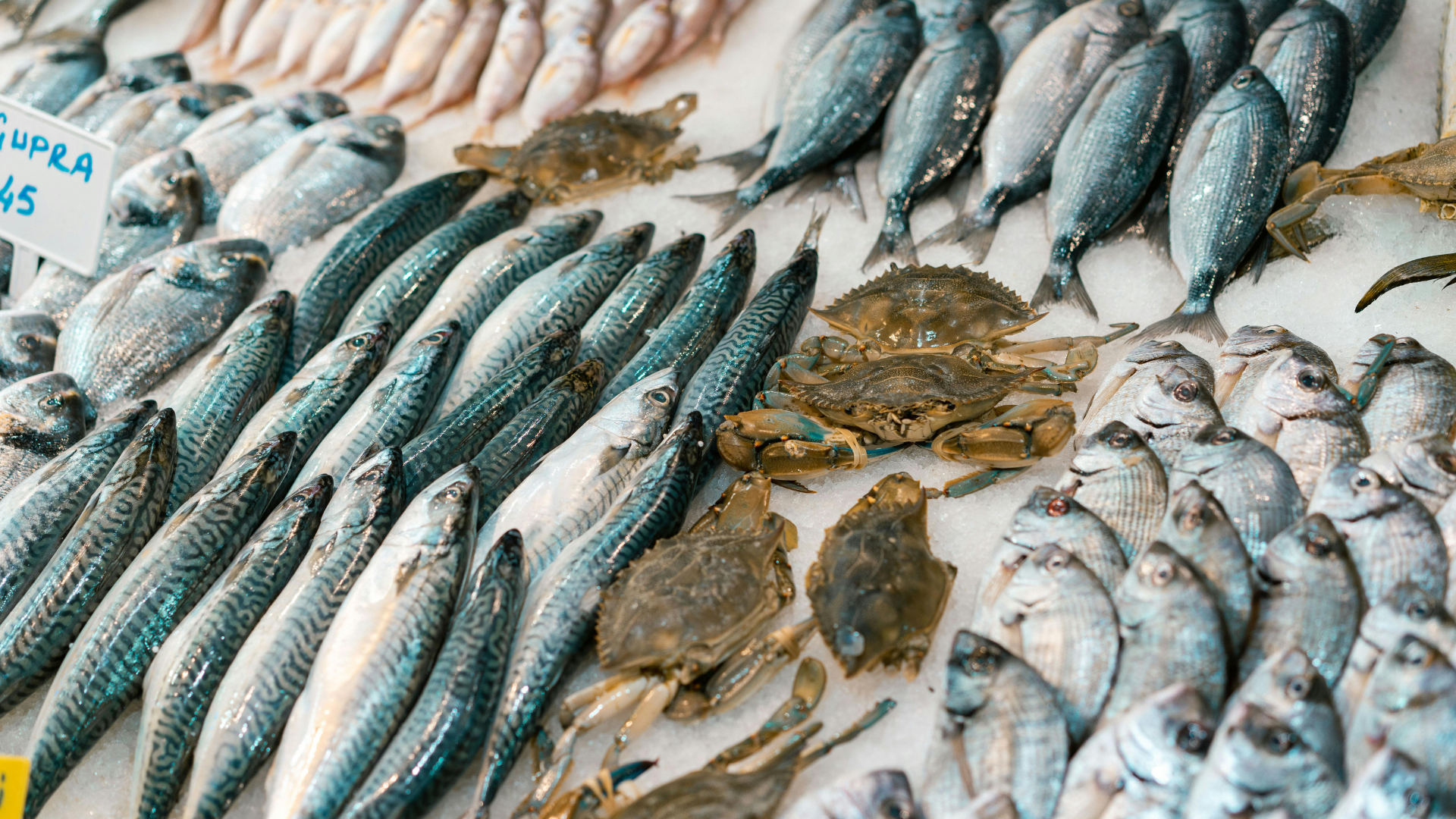 Fresh fish displayed on ice at a market, with crabs in the center.