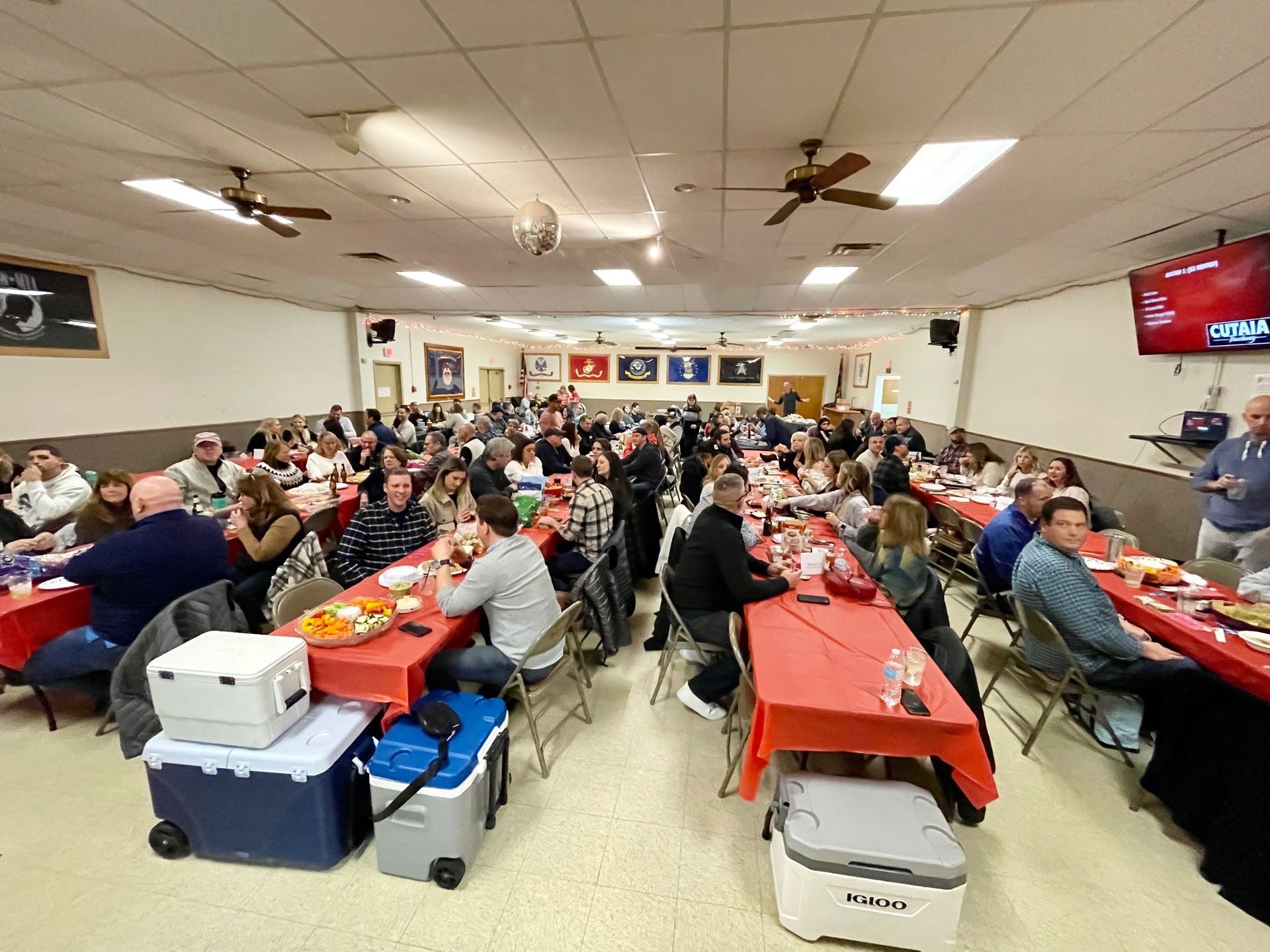 A large group of people are sitting at long tables in a large room.