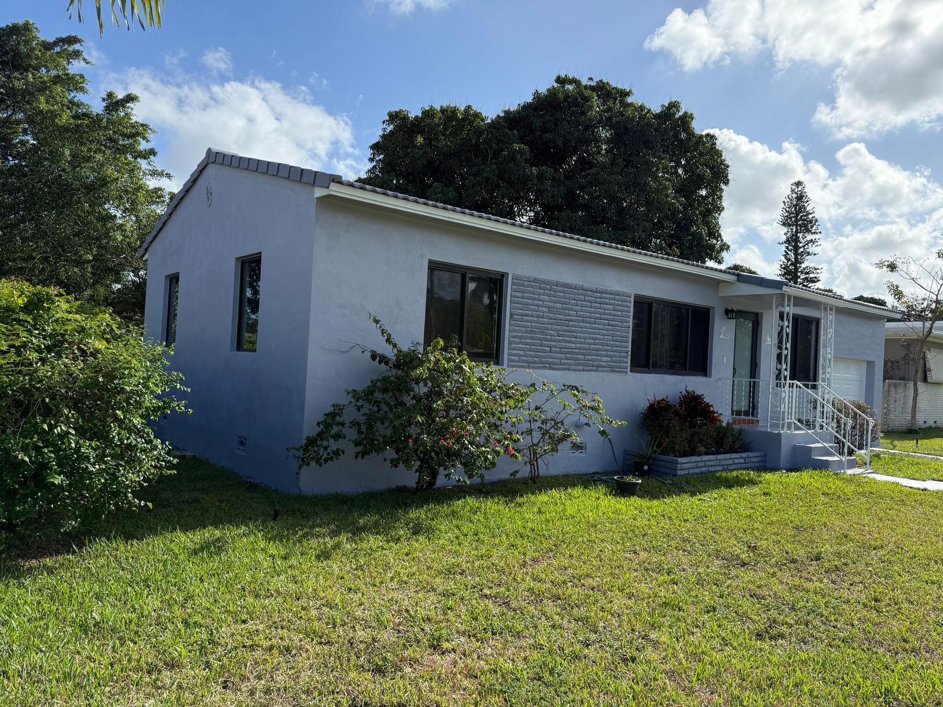 Gray house with windows, front door, and a small porch on a grassy lawn under a partly cloudy sky.