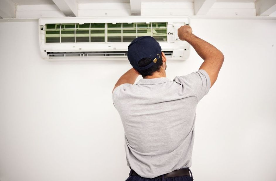 Worker installing a wall-mounted air conditioner indoors with a tool