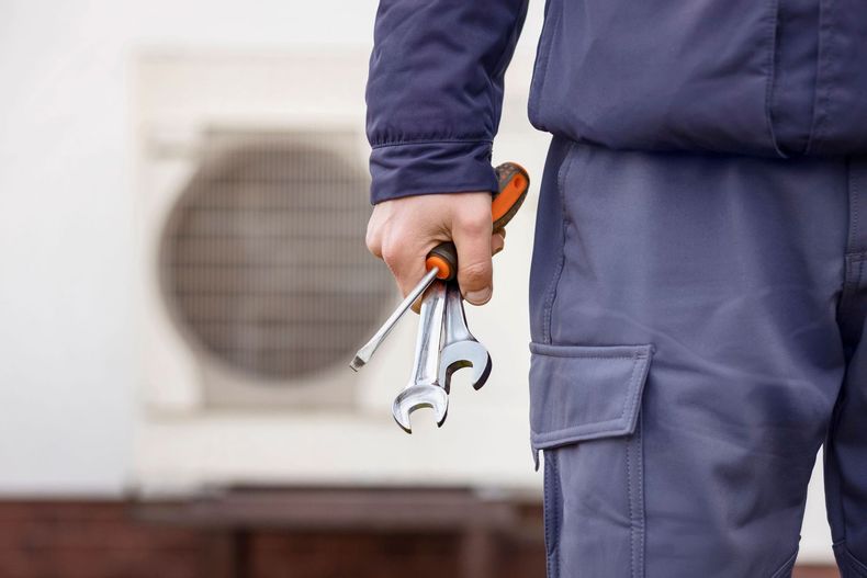 Handyman holding a wrench and screwdriver beside an outdoor air conditioner unit