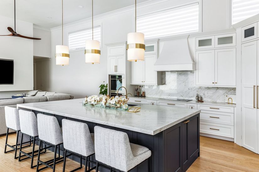 Bright modern kitchen with a large marble island, white cabinets, pendant lights, and barstools