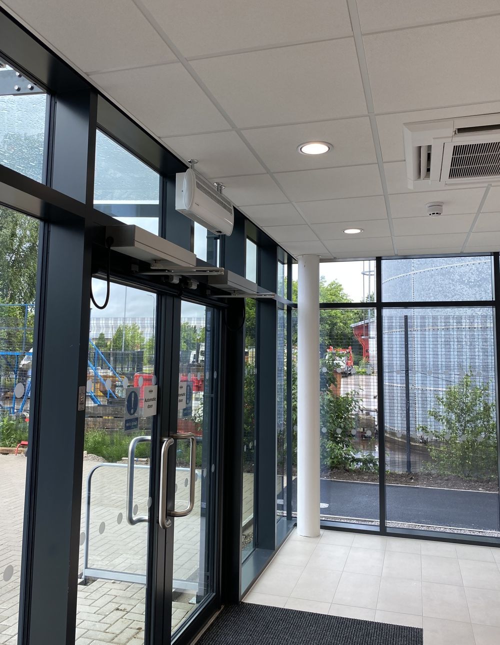 Automatic door in a glass doorway, with push bars and overhead closer. Interior hallway with tiled ceiling.