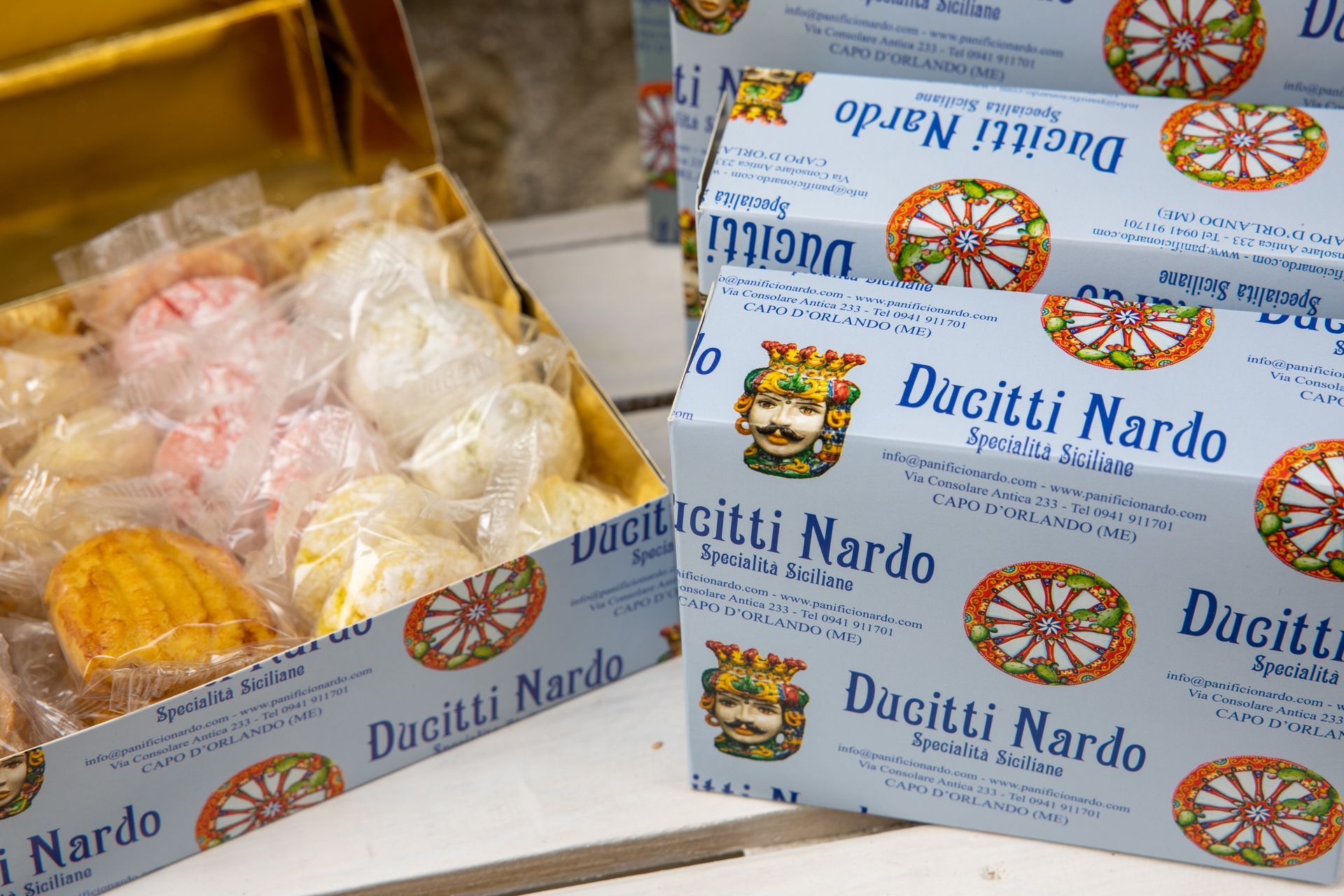 Scatole di dolciumi Ducitti Nardo in vari colori; scatola blu con motivo floreale e logo.