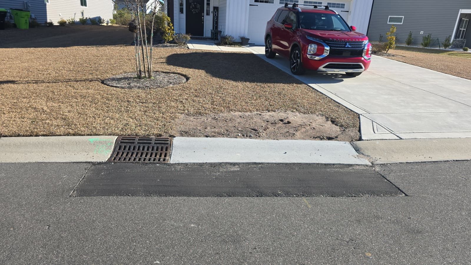 Driveway with a red SUV parked beside a gravel yard and curb drain in front of a house