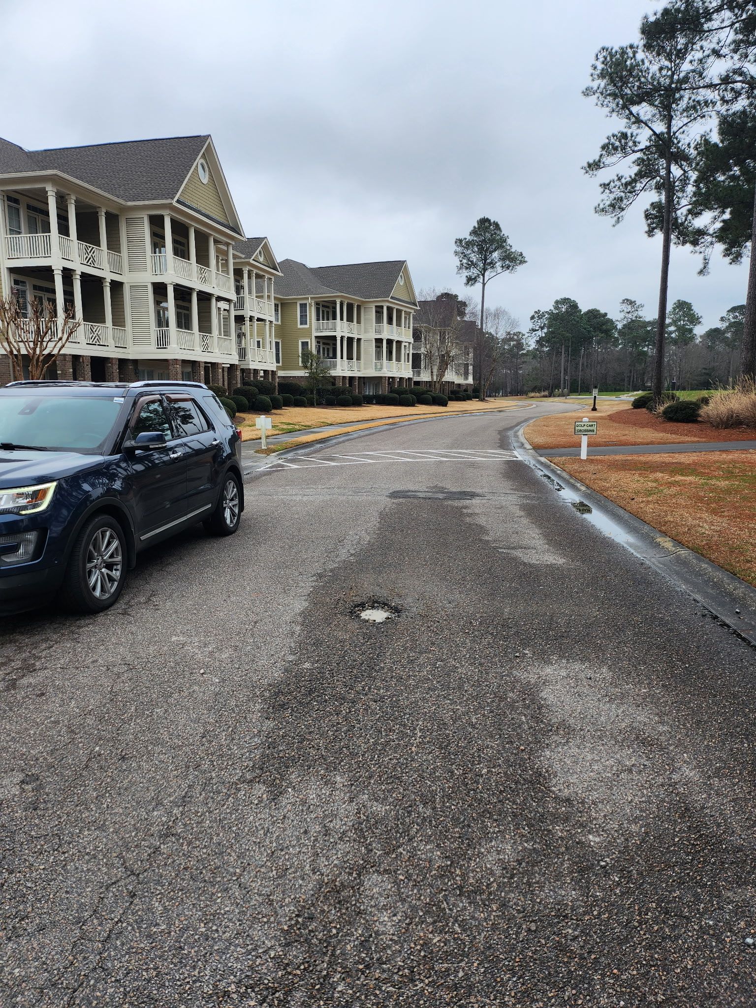 Apartment complex under construction beside a gravel road, with a parked black SUV and overcast sky.