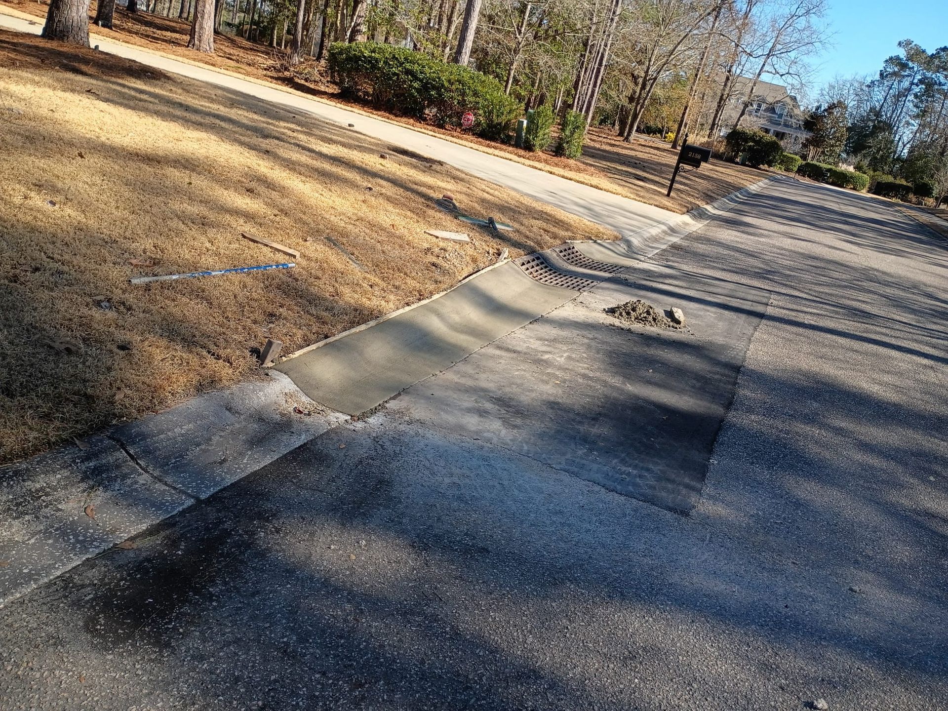 Cracked sidewalk beside a dry grassy area and trees along a quiet road