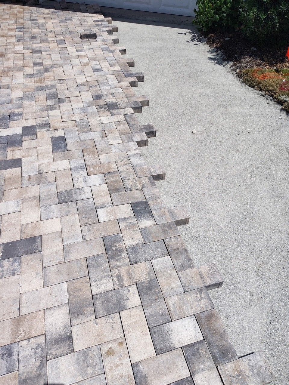 Stone paver walkway beside a light gravel path with edging stones and shrubs along the side