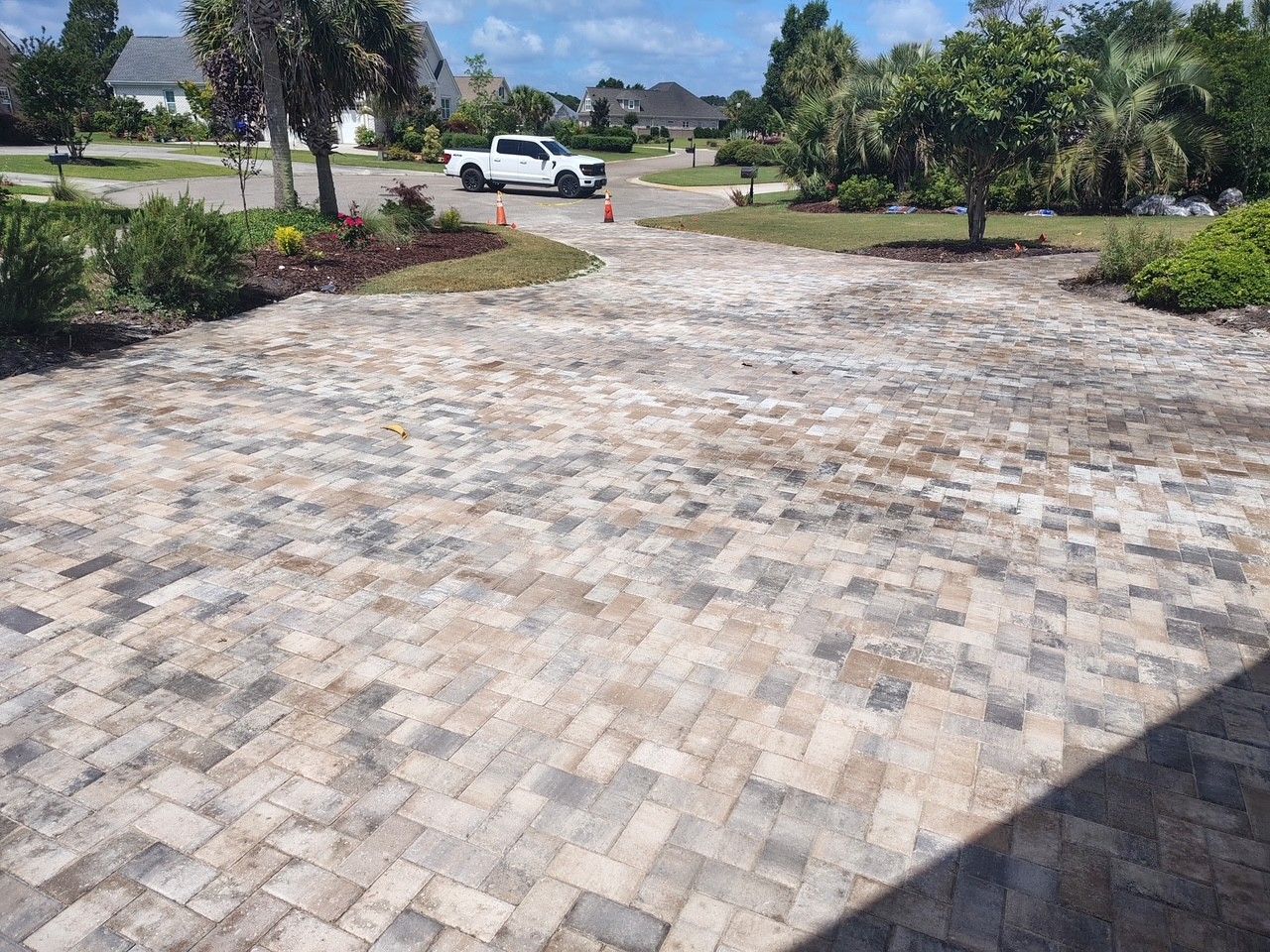 Brick-paved driveway with a white pickup truck and trees in a sunny suburban yard