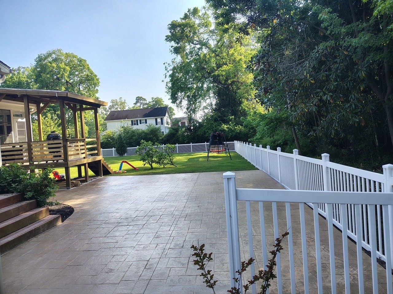 Patio path beside a white fence leading to a shaded gazebo in a green backyard