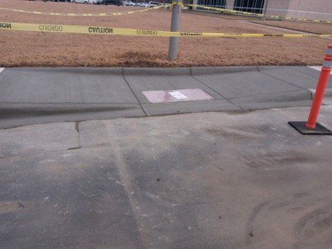 Caution tape and orange cones block a sidewalk near a construction site and curb ramp.