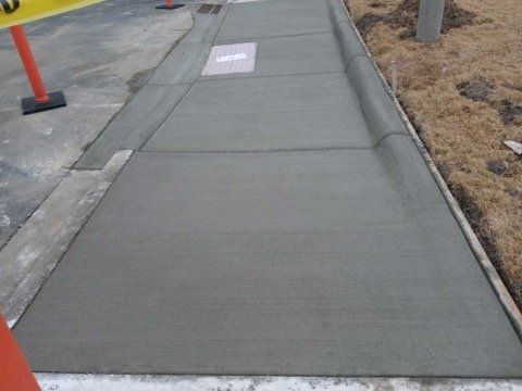 New concrete sidewalk beside a road, with a small sign and orange cones nearby.