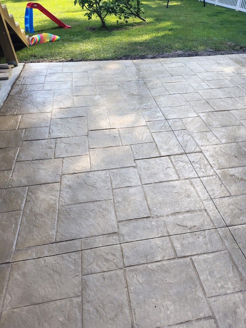 Stone patio leading to a grassy backyard with a red-and-blue slide in the distance.
