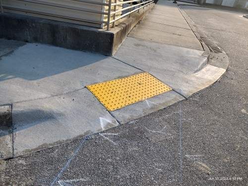 Sidewalk corner with a yellow tactile curb ramp at the edge of a street.
