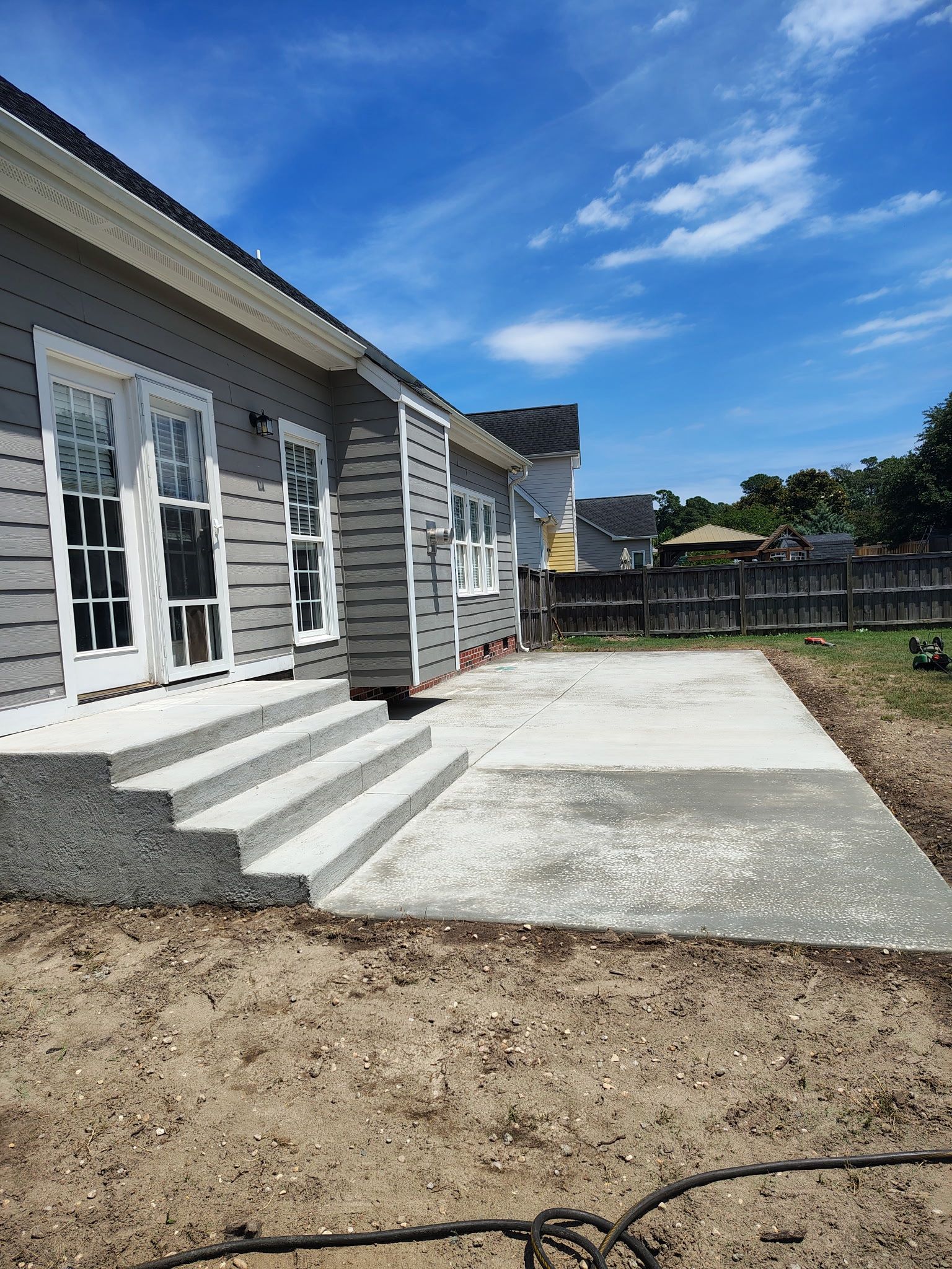 House exterior with white-trimmed doors, concrete steps, and a newly poured patio under a blue sky