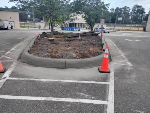Damaged asphalt around a raised concrete island, marked by orange traffic cones in a parking lot.