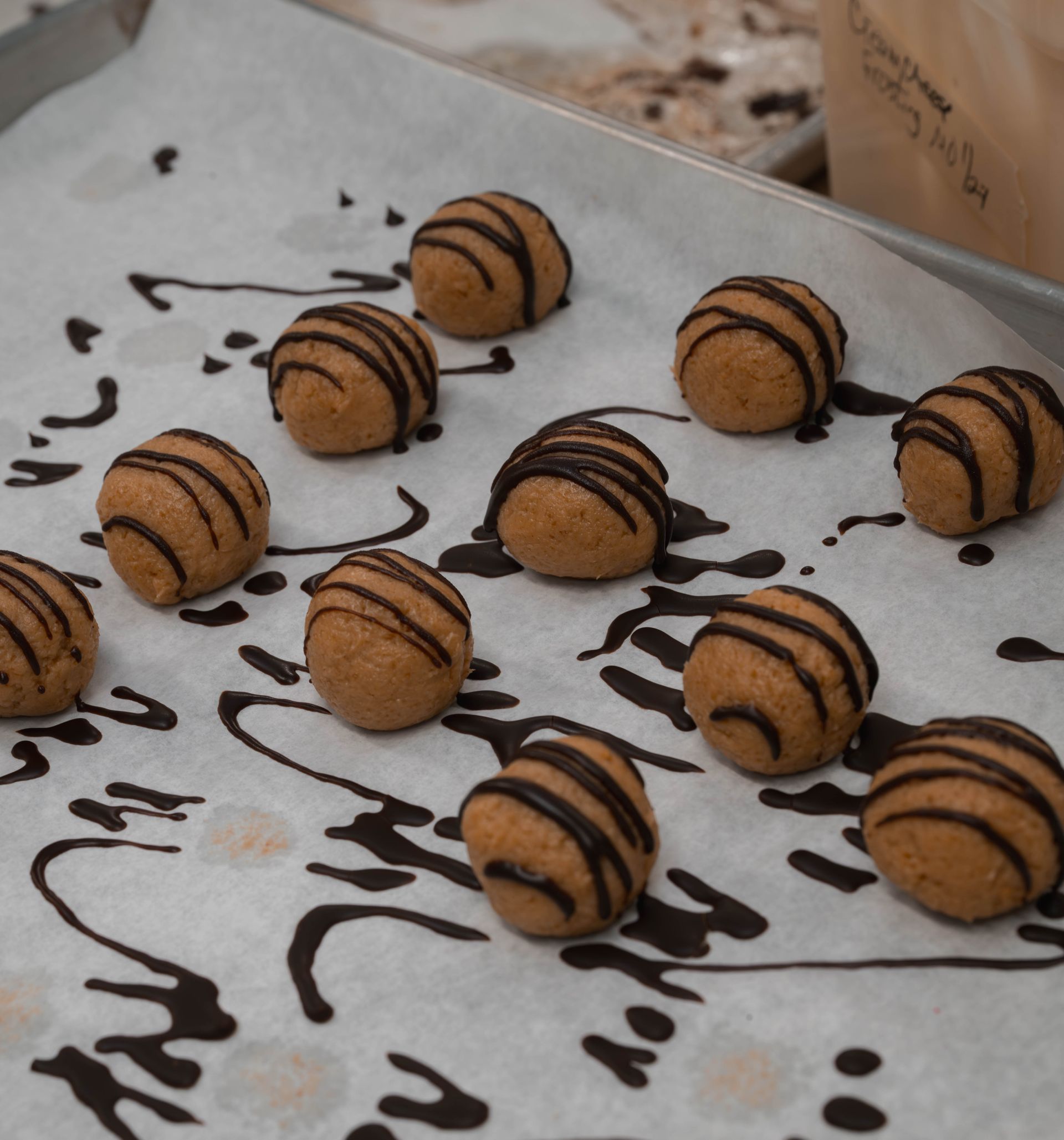 Chocolate-drizzled cookie balls on parchment paper, arranged in rows with scattered chocolate drizzle.
