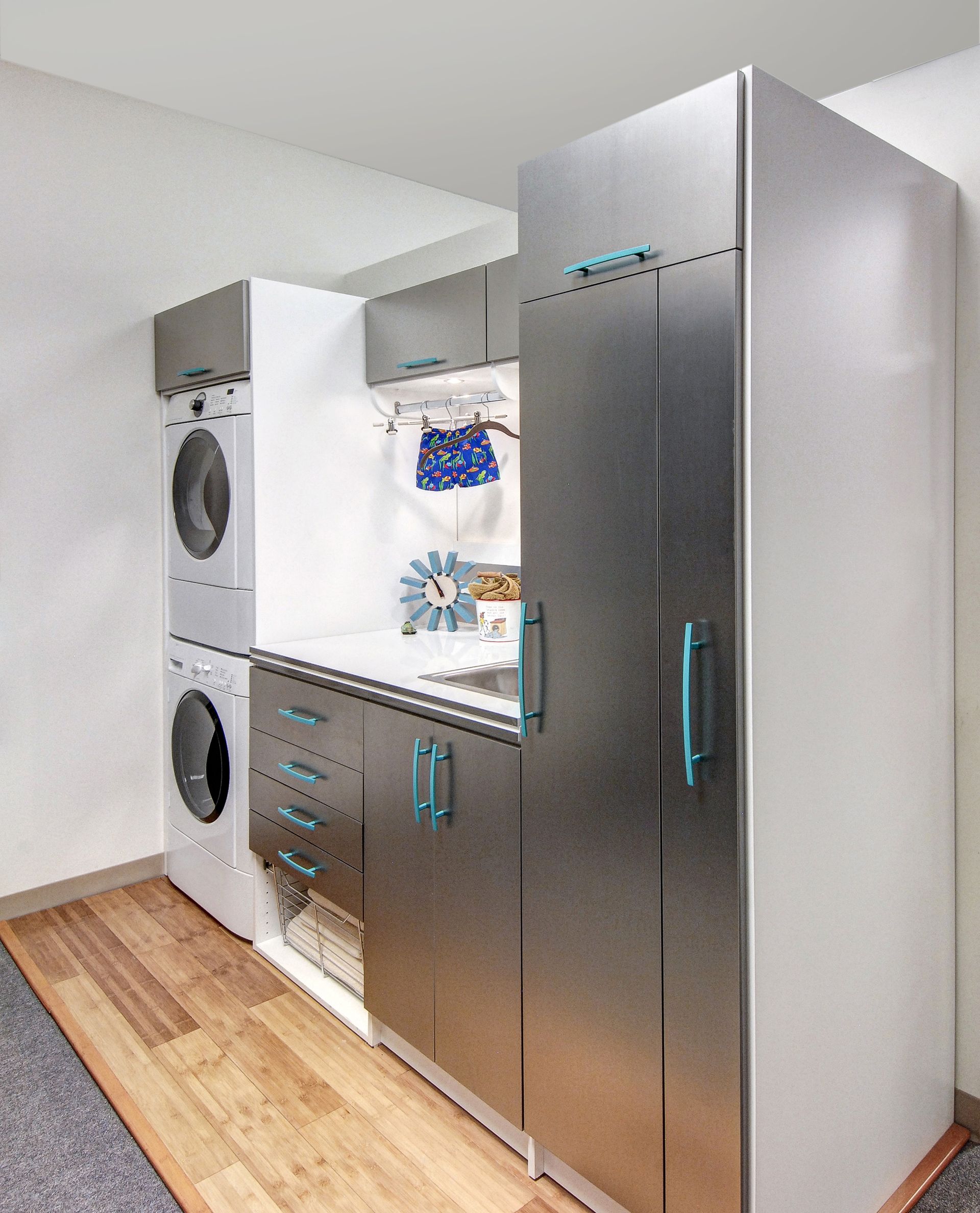 Modern laundry room with stacked washer/dryer, stainless steel cabinets, and blue accents.
