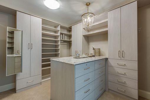A spacious walk-in closet featuring light wood cabinets, open shelving, and a central island with drawers and stone top.