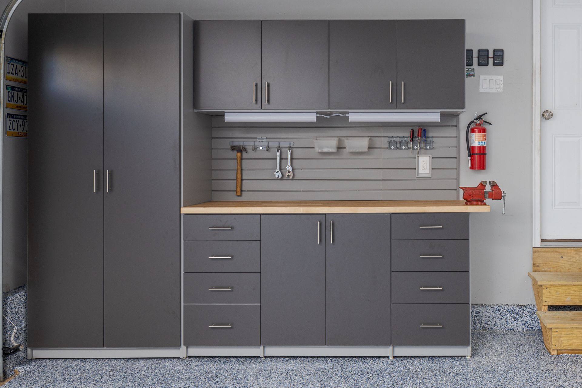 Organized white pantry shelving with various shelves, pull-out drawers, wire baskets, and hanging kitchen linens.