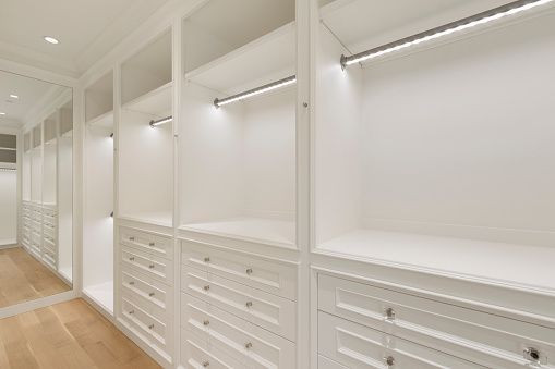 A bright, white walk-in closet featuring built-in cabinetry, drawers, hanging rods, and integrated LED lighting.