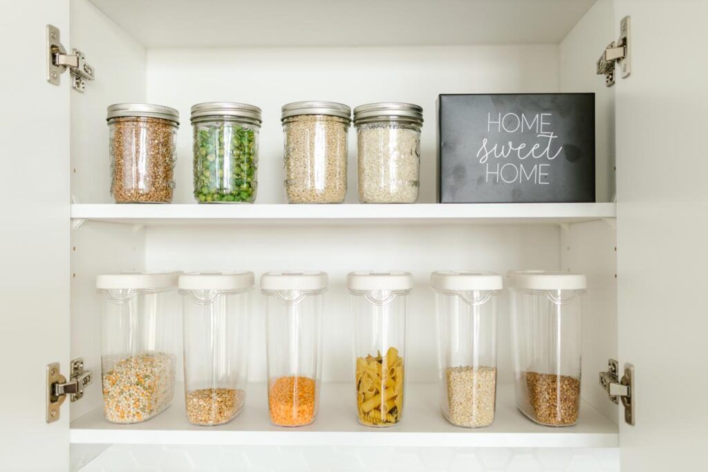 Two white pantry shelves filled with organized glass jars and rectangular storage containers containing dry goods.