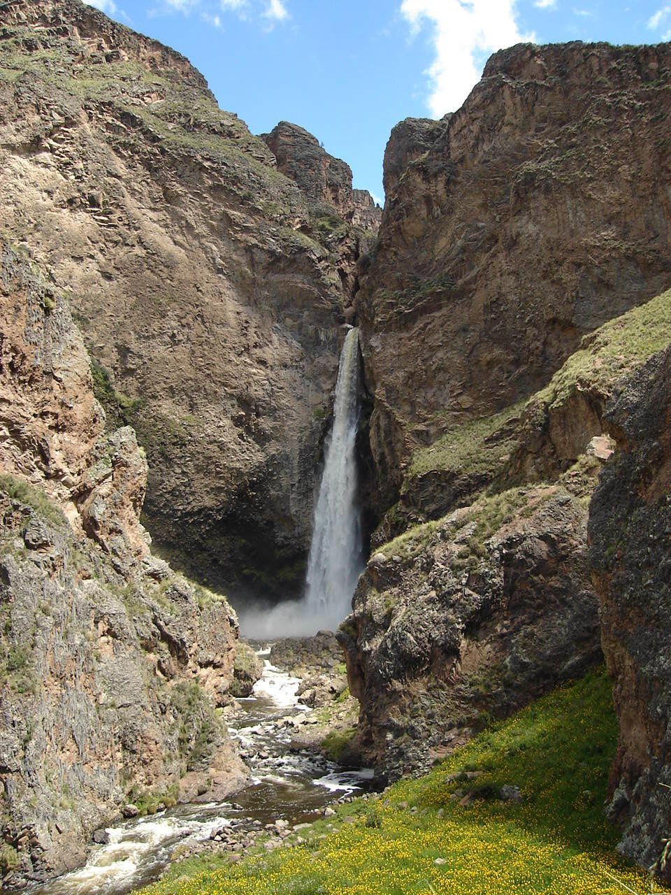 Una alta cascada se precipita entre las paredes rocosas del cañón hacia un estrecho arroyo.