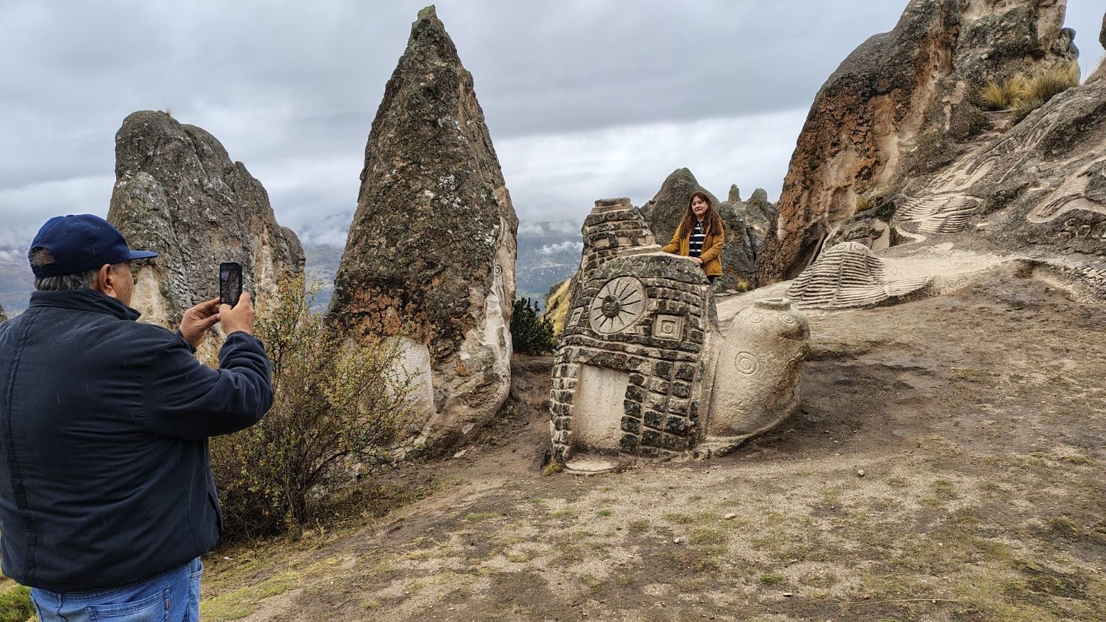 Persona fotografiando altos pilares de piedra y ruinas bajo un cielo nublado.