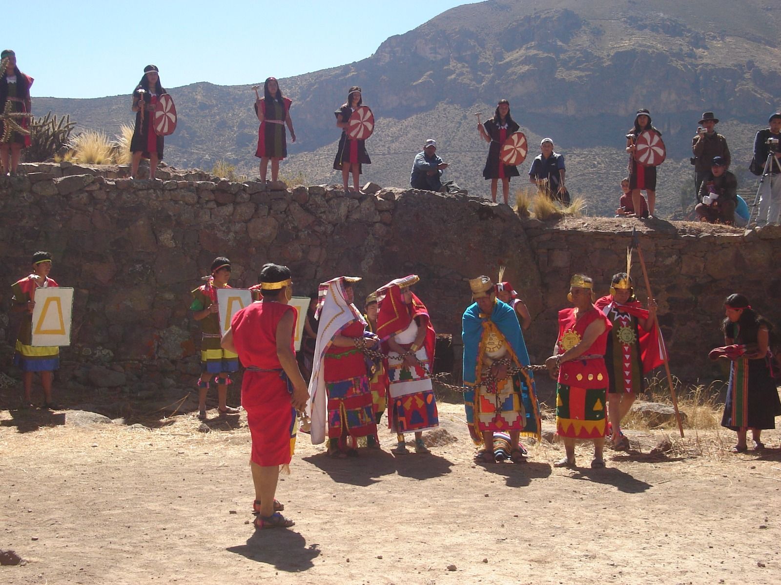 Grupo con coloridos trajes tradicionales actuando al aire libre con montañas de fondo.
