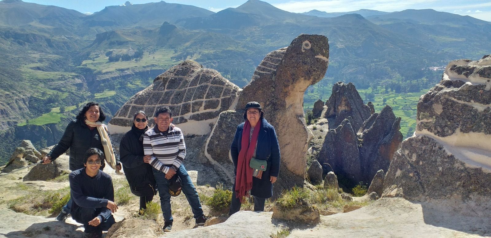 Cuatro personas posando sobre ruinas rocosas con montañas y un valle verde al fondo.