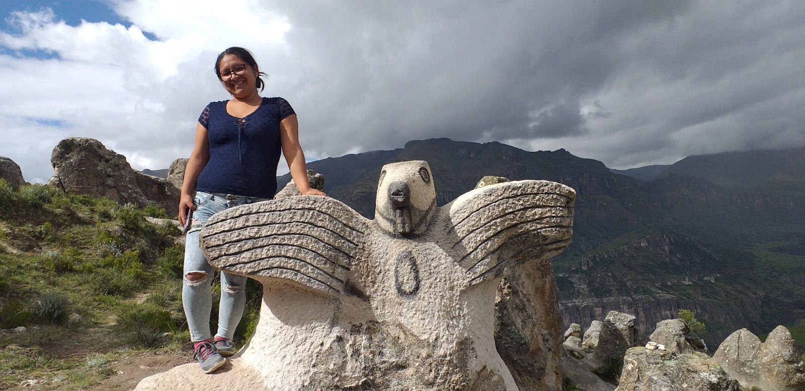 Una persona de pie junto a una estatua de piedra de un oso con las alas extendidas