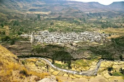 Pueblo de casas aterrazadas en la ladera de una colina, en un valle verde con una carretera sinuosa y montañas al fondo.