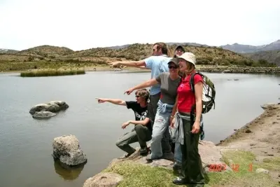 Grupo de excursionistas señalando al otro lado de un lago en un paisaje rocoso y montañoso.