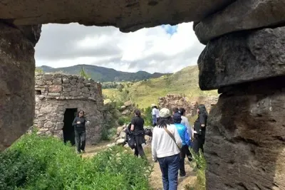 Visitantes paseando entre antiguas ruinas de piedra con verdes colinas al fondo.