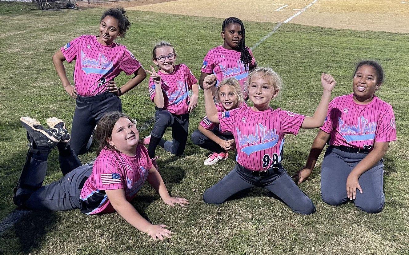 Group of youth soccer players posing on grass in pink jerseys after a game