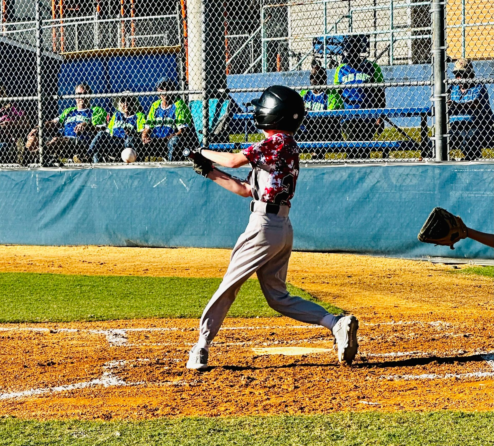 Baseball player in black helmet and red jersey swings at a pitch on a sunny field.