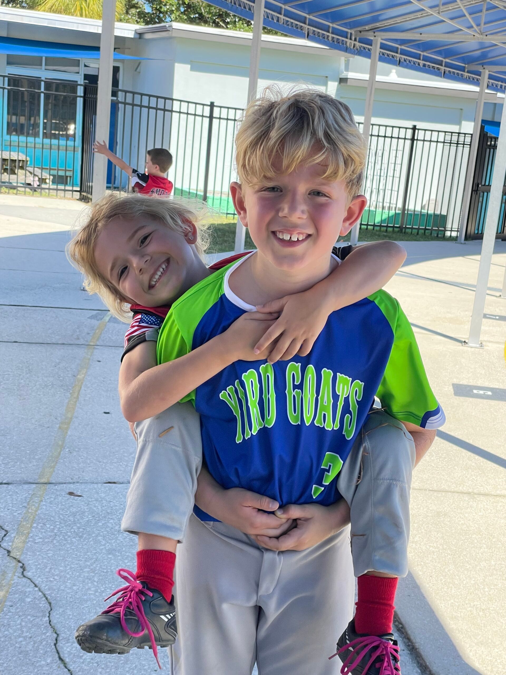 Two children smiling outdoors, one giving the other a piggyback ride on a school playground.
