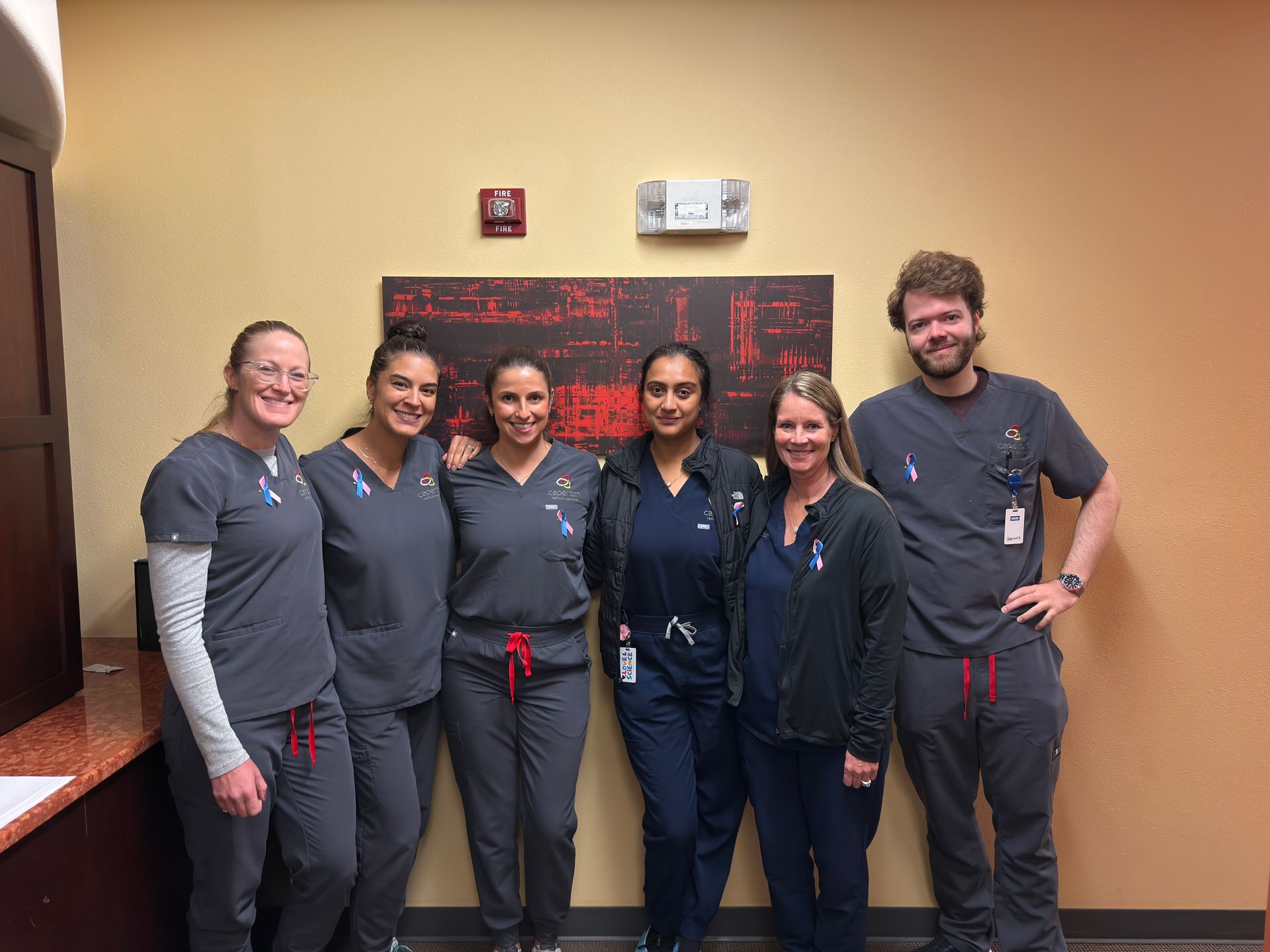 Medical staff pose for a photo in grey suits, and wearing pink and blue ribbon. 