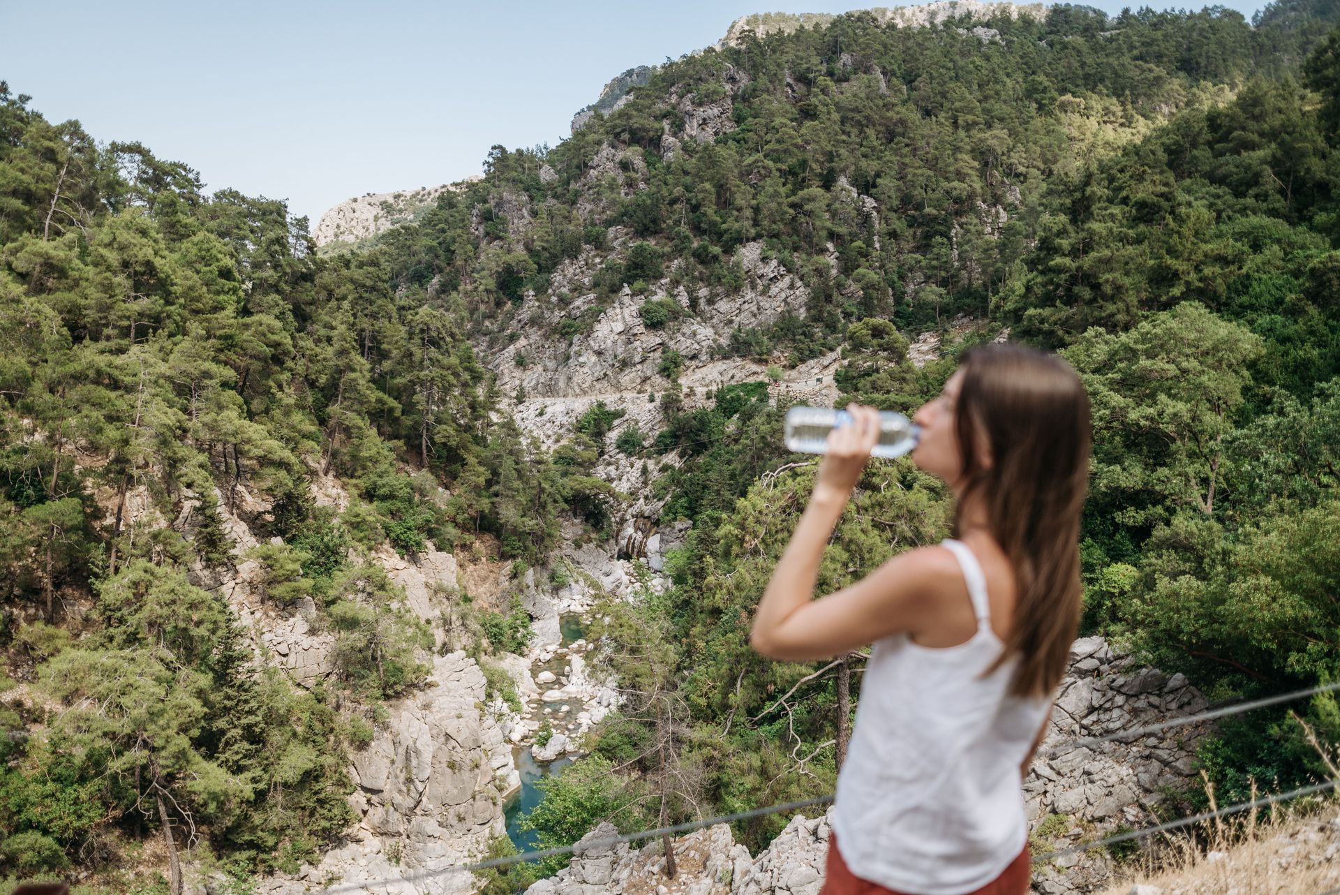 Woman drinking water while overlooking a lush green mountain ravine
