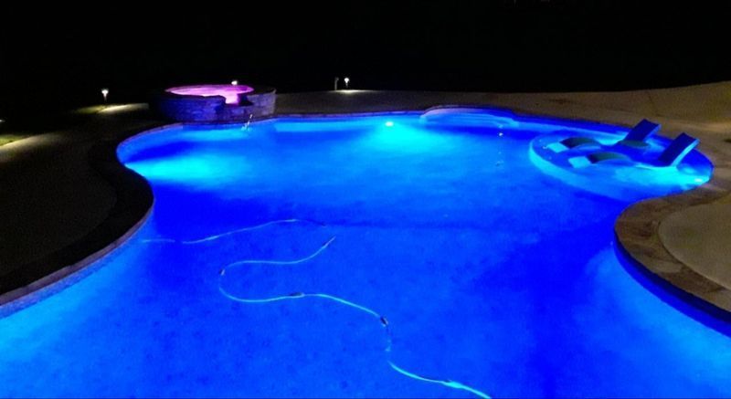 A large swimming pool is lit up at night with blue lights.