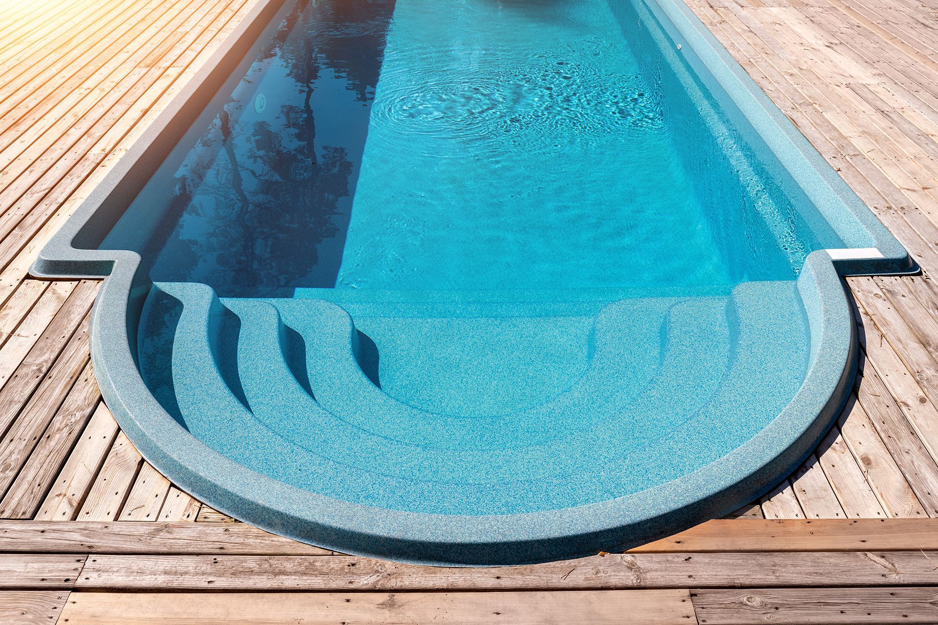 A large swimming pool is sitting on top of a wooden deck.