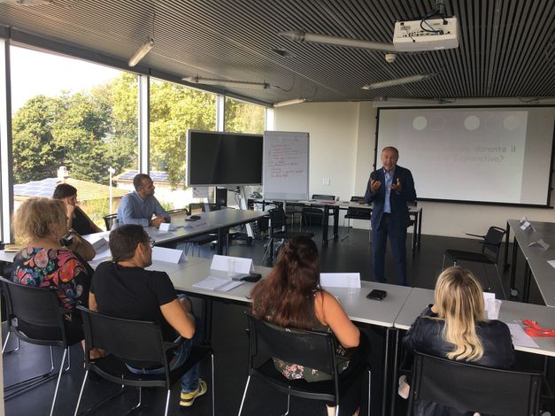 Il relatore terrà una presentazione in un'area esterna coperta adibita a riunioni, con pubblico seduto, proiettore e schermi.