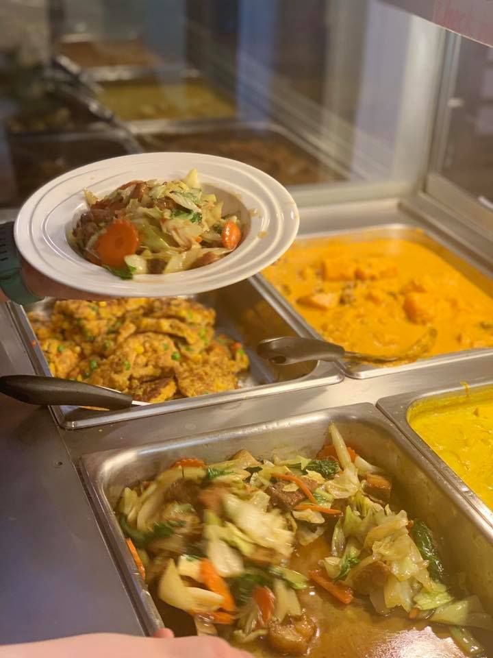 A person is holding a plate of food over a buffet line of food.