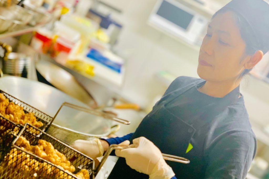 A woman is cooking chicken in a fryer in a kitchen.